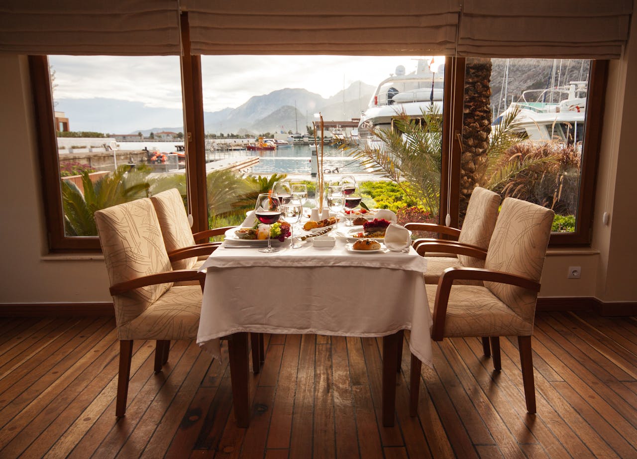 services-01 Elegantly set table in a seaside restaurant with a marina view, featuring gourmet dishes and fine dining setup.