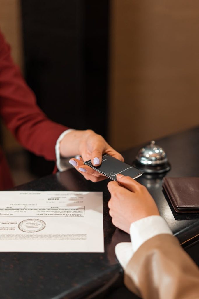 pexels photo 7820321 A hotel receptionist hands a key card to a guest over the counter, with documents visible.